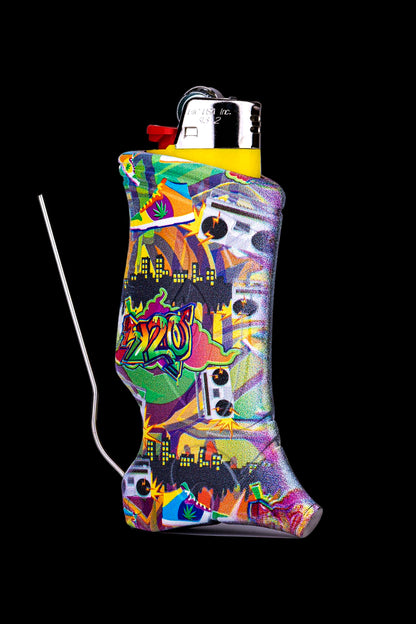 A colorful, patterned lighter sleeve covering a silver lighter with a metal cleaning tool alongside it, against a black background.