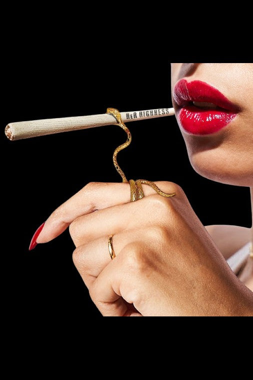 Close-up of a hand with red nails holding a lit cannabis joint, with lips visible in the background.