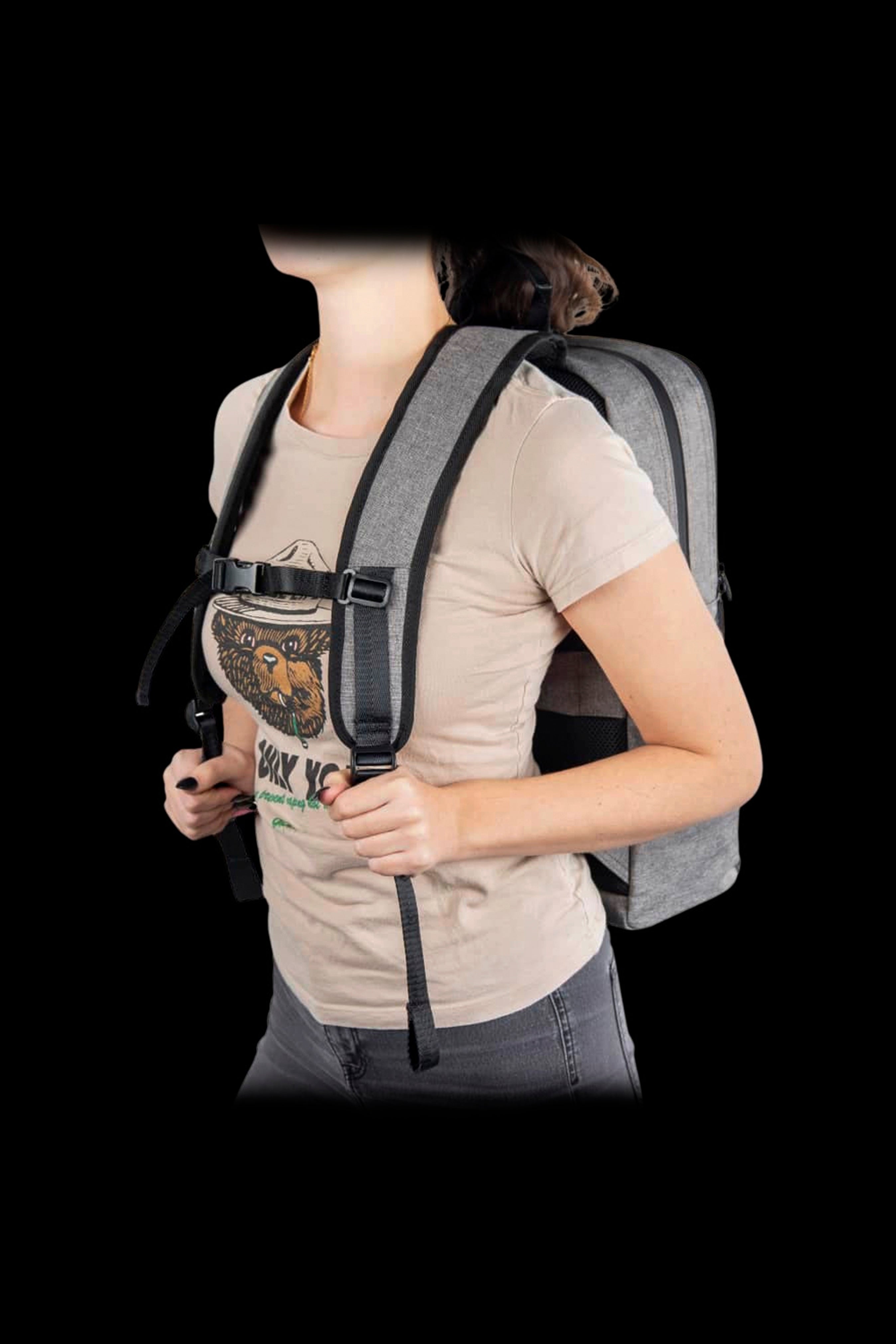 Three-quarter view of a person wearing a gray Ooze Traveler Smell Proof Backpack with padded straps and chest buckle against a black background