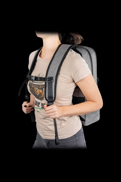 Three-quarter view of a person wearing a gray Ooze Traveler Smell Proof Backpack with padded straps and chest buckle against a black background