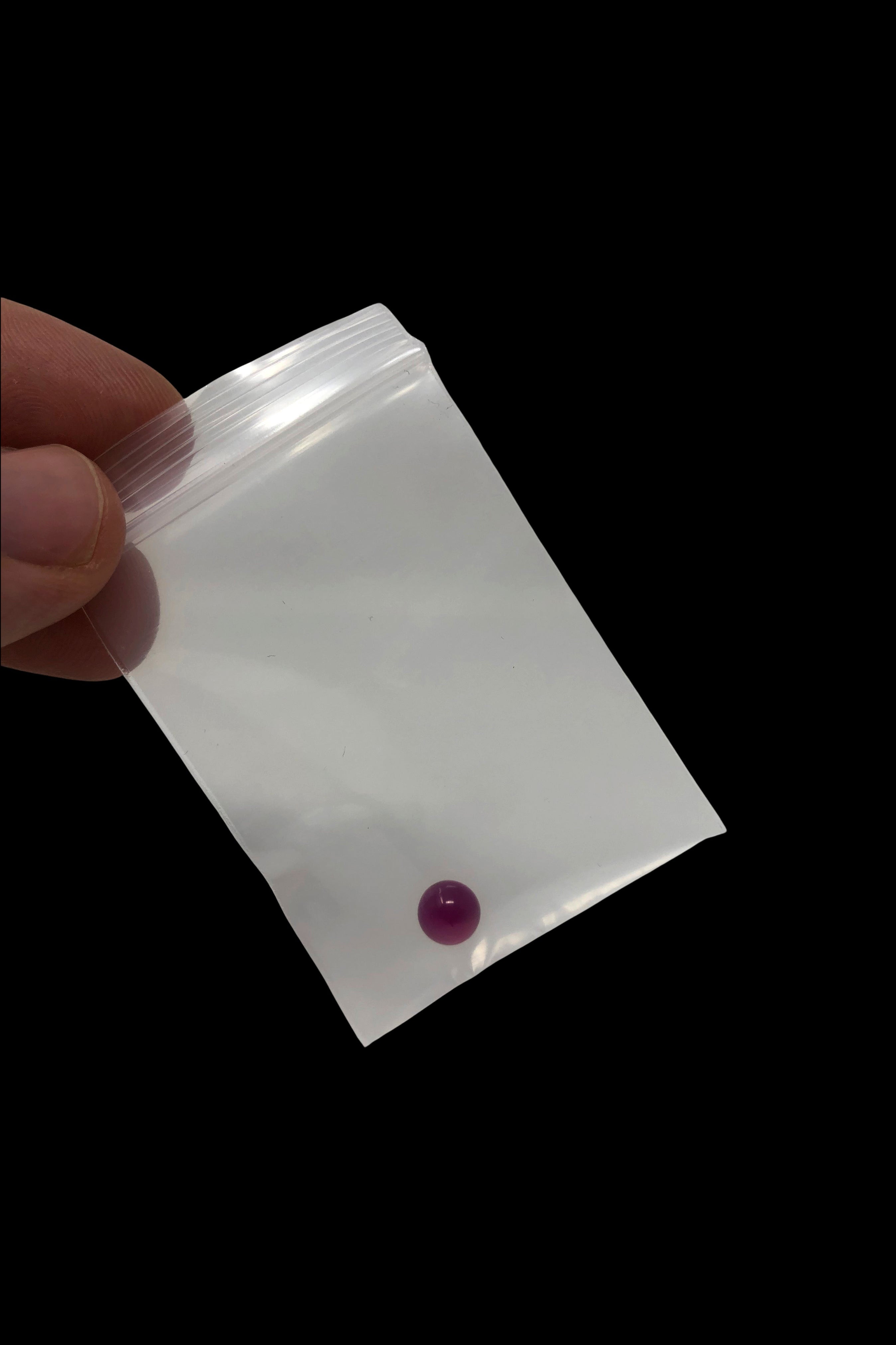 Purple cannabis rosin pearl in a clear plastic bag, held by a hand.