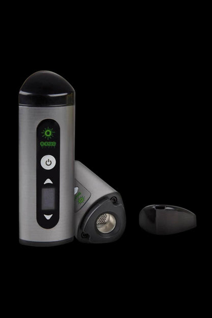 Silver and black cannabis vaporizer with illuminated green controls, displayed with open chamber.