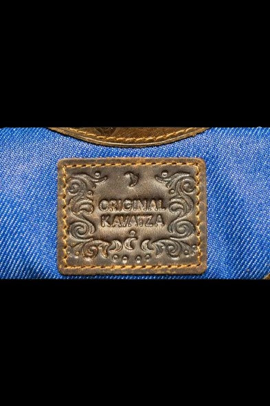 Close-up of a blue denim bag with a distressed leather patch embossed with "ORIGINAL KAVATZA."
