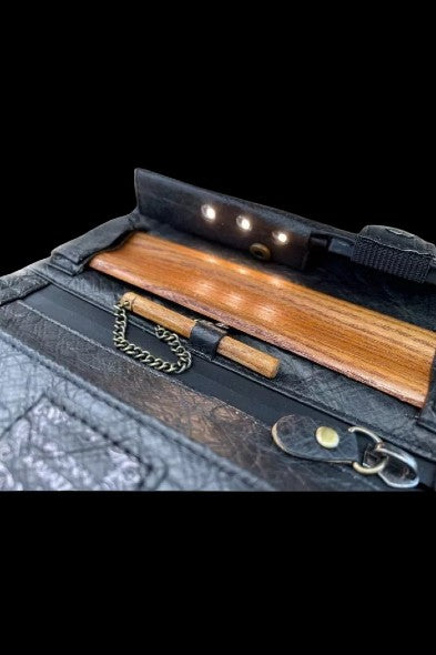Black cannabis accessory case open, revealing a wooden rolling tray and gold-tone chain.