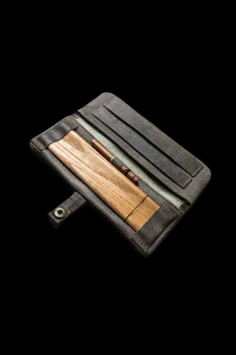 Wooden pipe and cleaning brush neatly stored in a black leather case, against a black background.