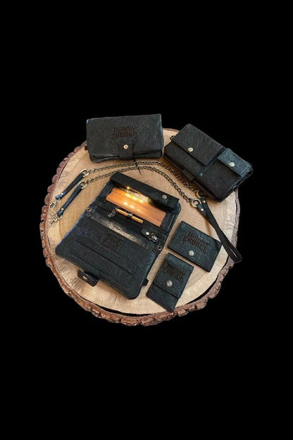Black leather cannabis accessories—cases, pouches, and a smell-proof bag—arranged on a wooden slice against a black background.