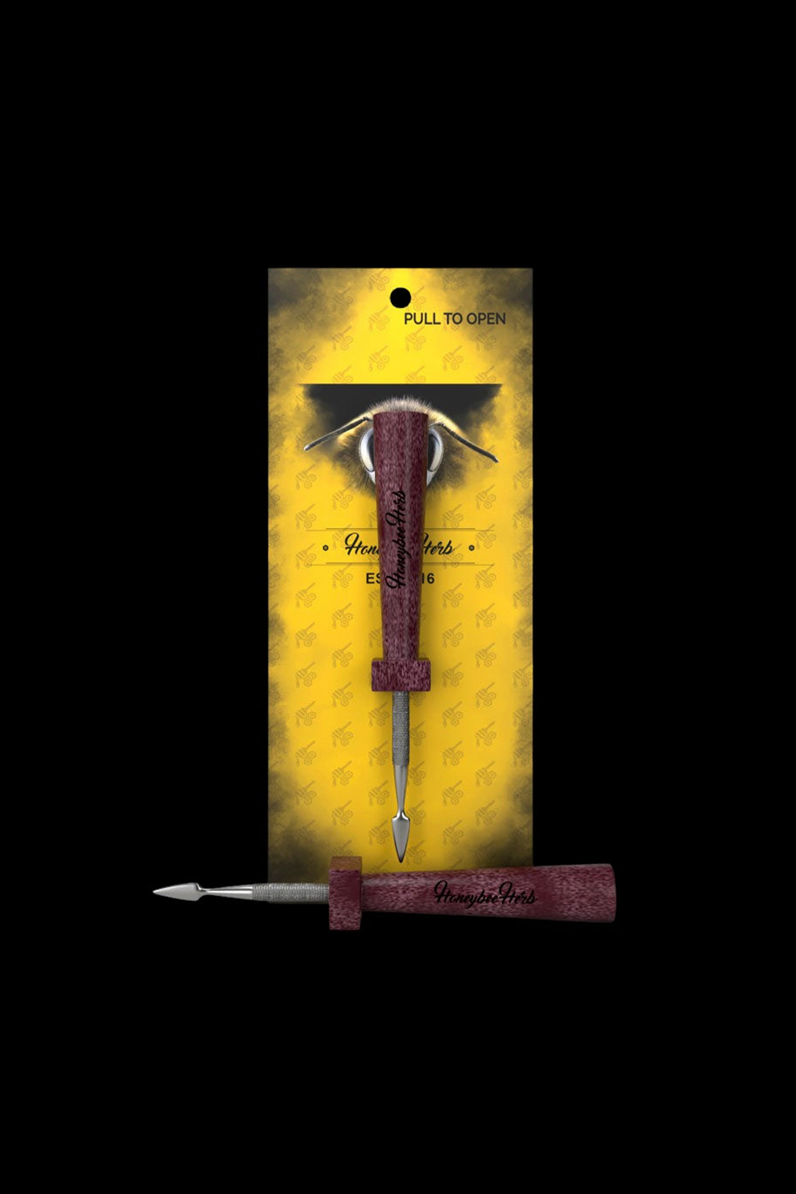 A packaged, ornate cannabis dab tool with a burgundy handle and golden bee-patterned background.