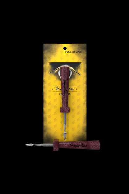 A packaged, ornate cannabis dab tool with a burgundy handle and golden bee-patterned background.