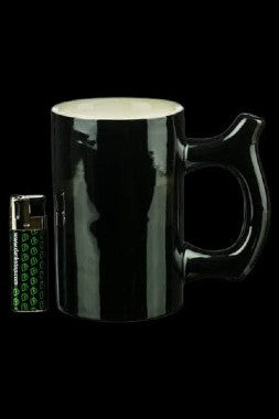 Black ceramic mug with a curved handle, positioned next to a small, green-labeled cannabis-themed electronic device.
