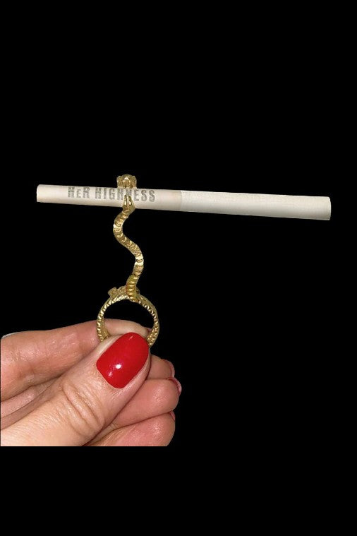 A hand with red nail polish holds a lit joint with a gold snake-shaped ring around it, reading "Her Highness."