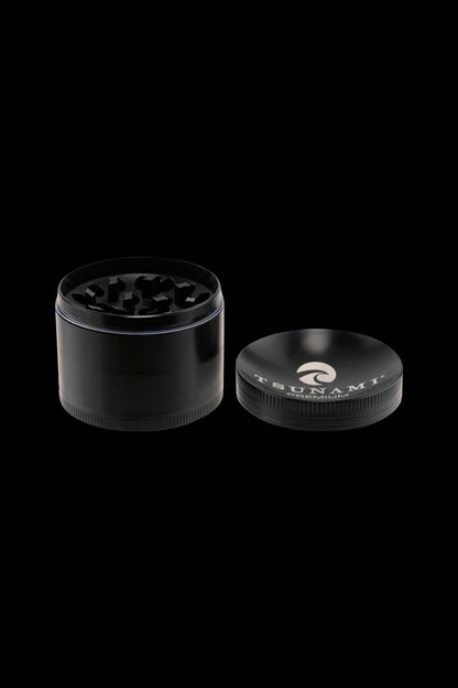 Black four-piece cannabis grinder with metal teeth, open to reveal ground herbs.