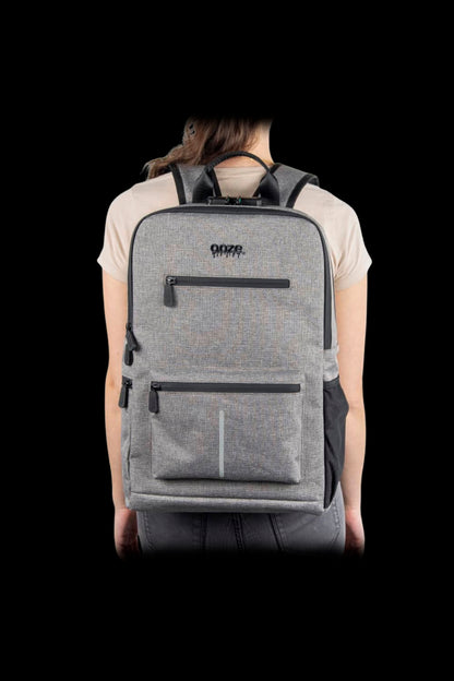 Rear view of a person wearing the gray Ooze Traveler Smell Proof Backpack against a black background, showing padded straps and front zip pockets.