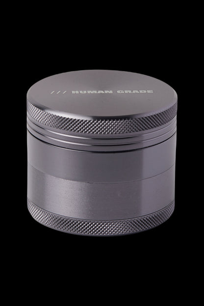 Black four-piece metal grinder with “HUMAN GRADE” etched on the lid.