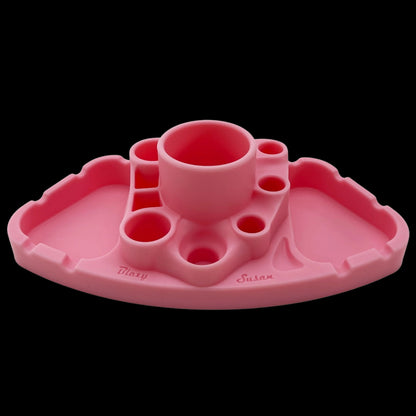 Low-angle front view of the pink Blazy Susan Deluxe Dab Station showing its central cup, multiple surrounding wells, and scalloped edge against a black background.