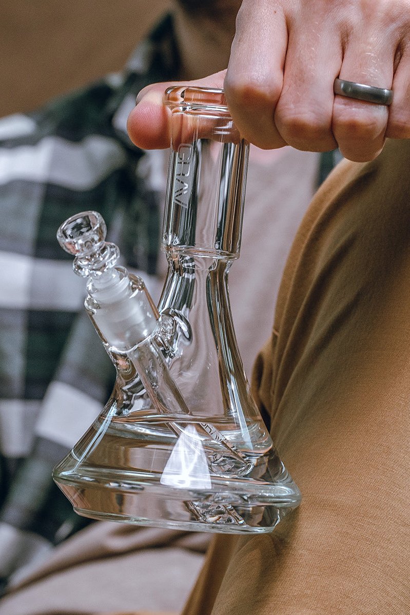 A person holding a clear glass bong with a downstem and water visible inside.