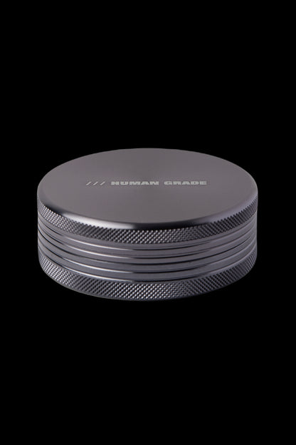 Black metal cannabis grinder with "HUMAN GRADE" engraved on top.