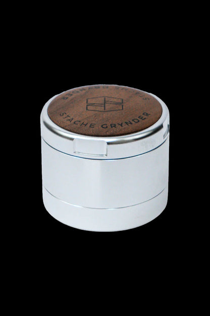 Silver cannabis grinder with a brown wooden top, branded "Stache Grynder".