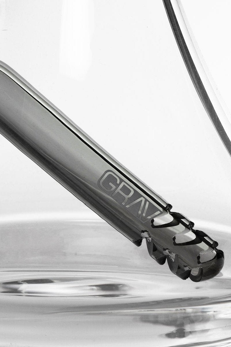 Close-up of a glass cannabis water pipe with the brand name "GRAV" visible, partially submerged in rippling water.