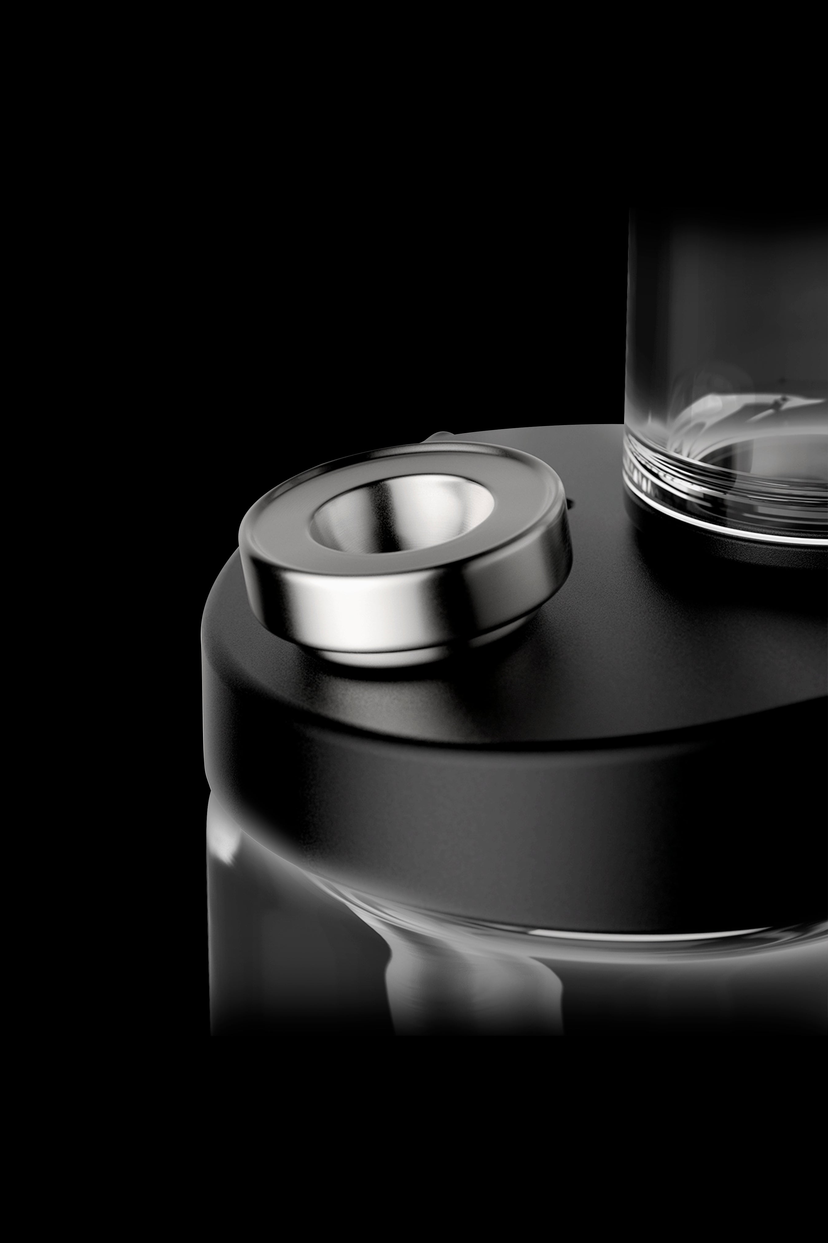 Close-up of a cannabis vape pen's metallic button and glass cartridge against a black background.