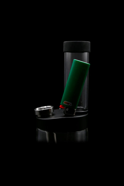 Black cannabis rig with a green lighter inside a clear glass chamber, reflected on a dark surface.
