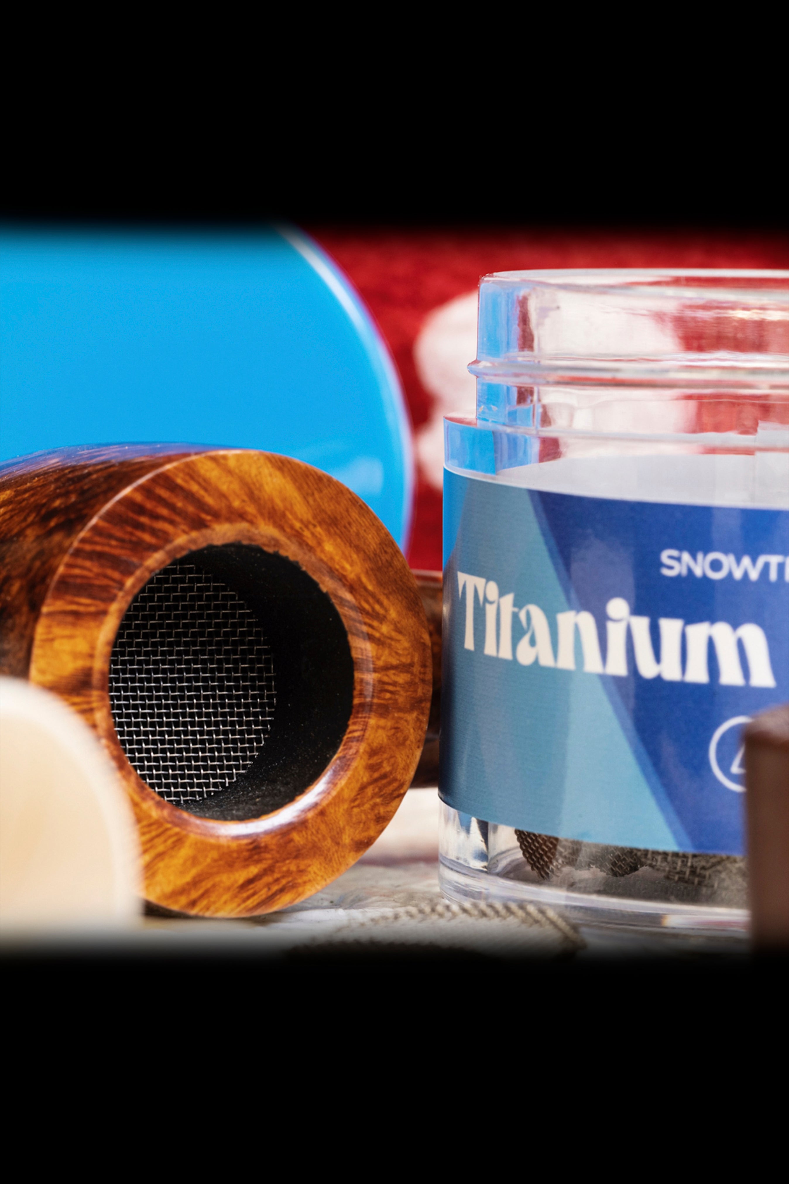 Close-up of a wooden pipe and a jar labeled “Titanium” with a blue and red color scheme, likely cannabis accessories.