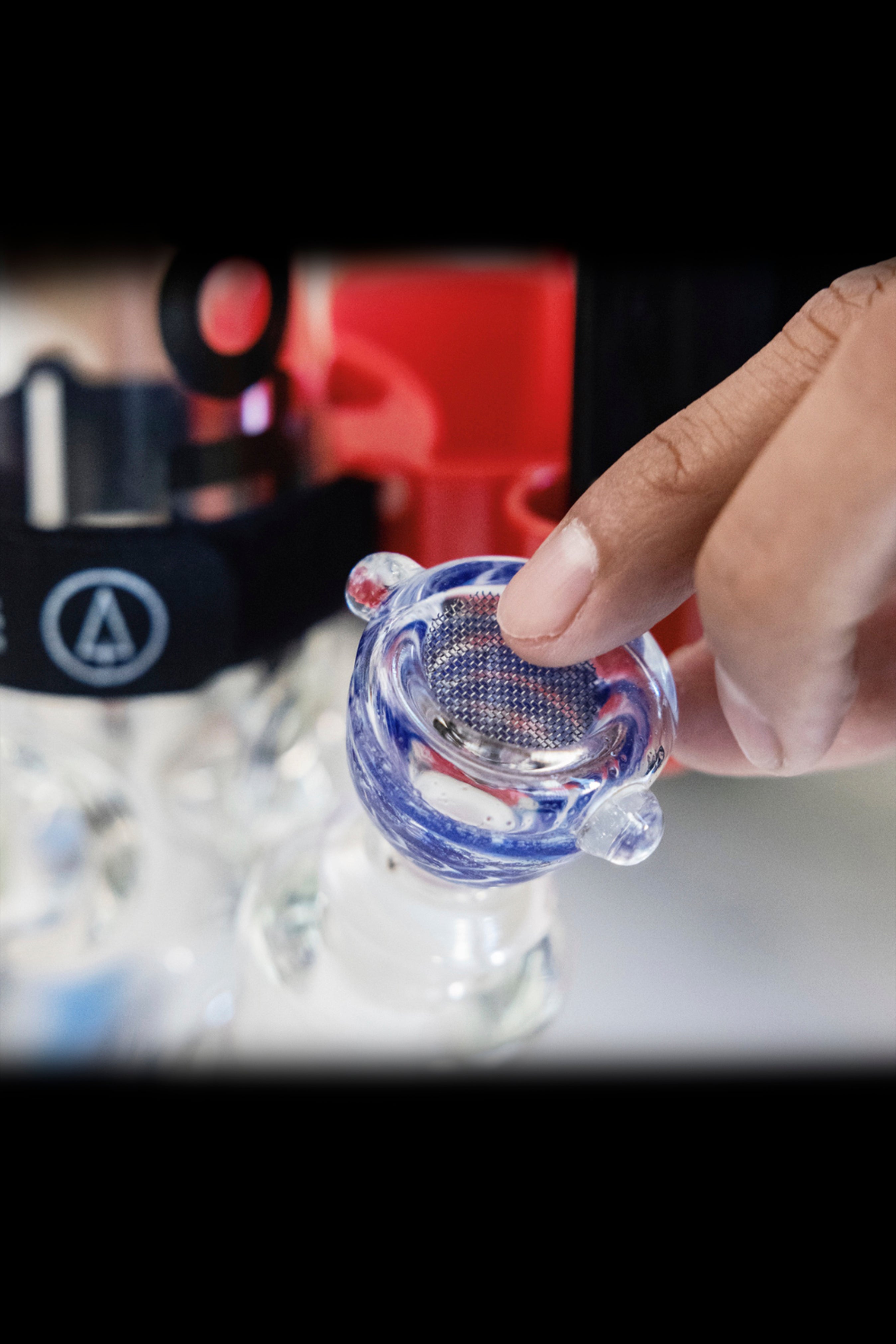 A hand holds a blue glass cannabis bowl over crushed ice.