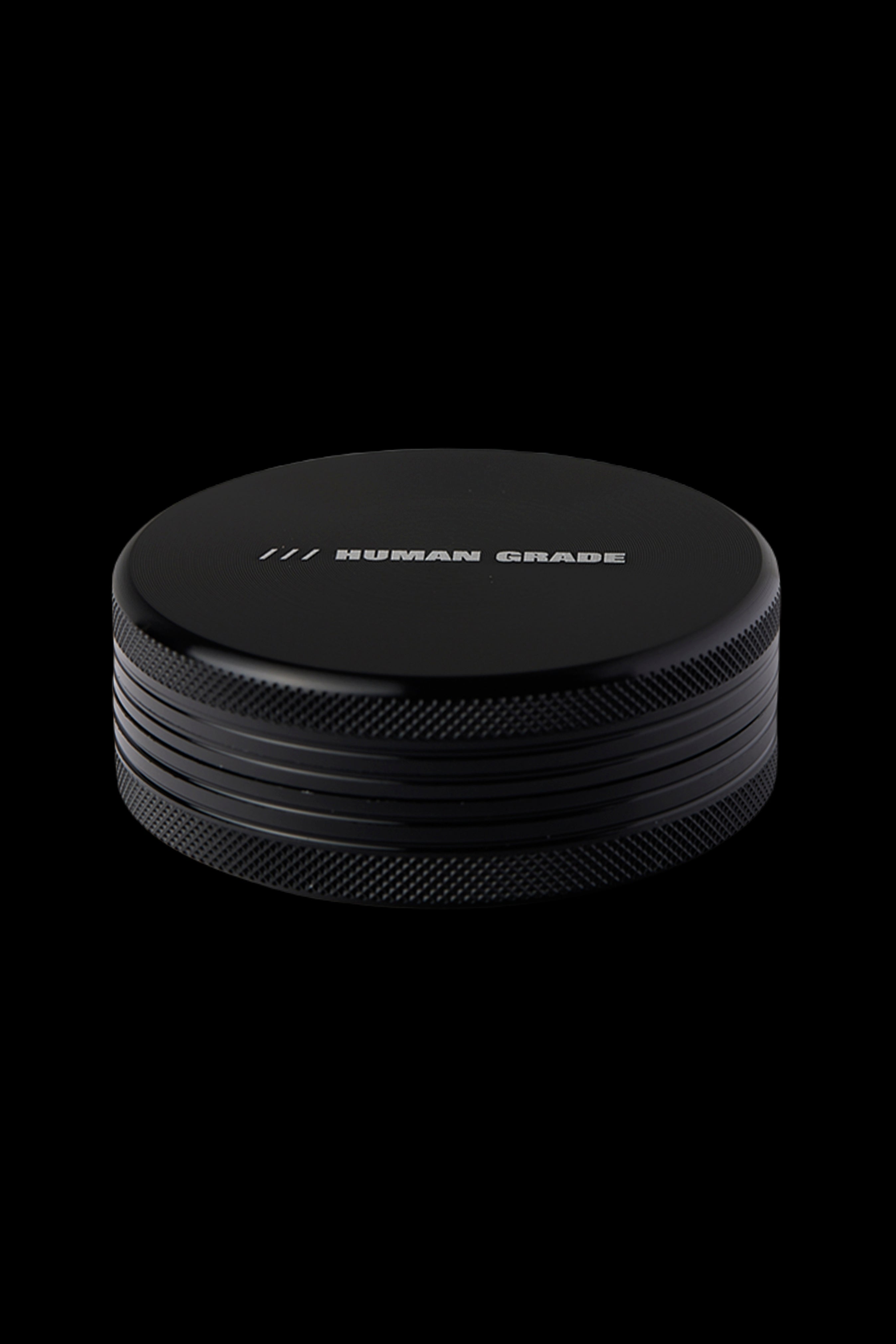 Black metal cannabis grinder with "HUMAN GRADE" etched on top.