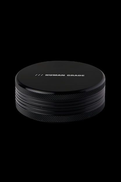 Black metal cannabis grinder with "HUMAN GRADE" etched on top.