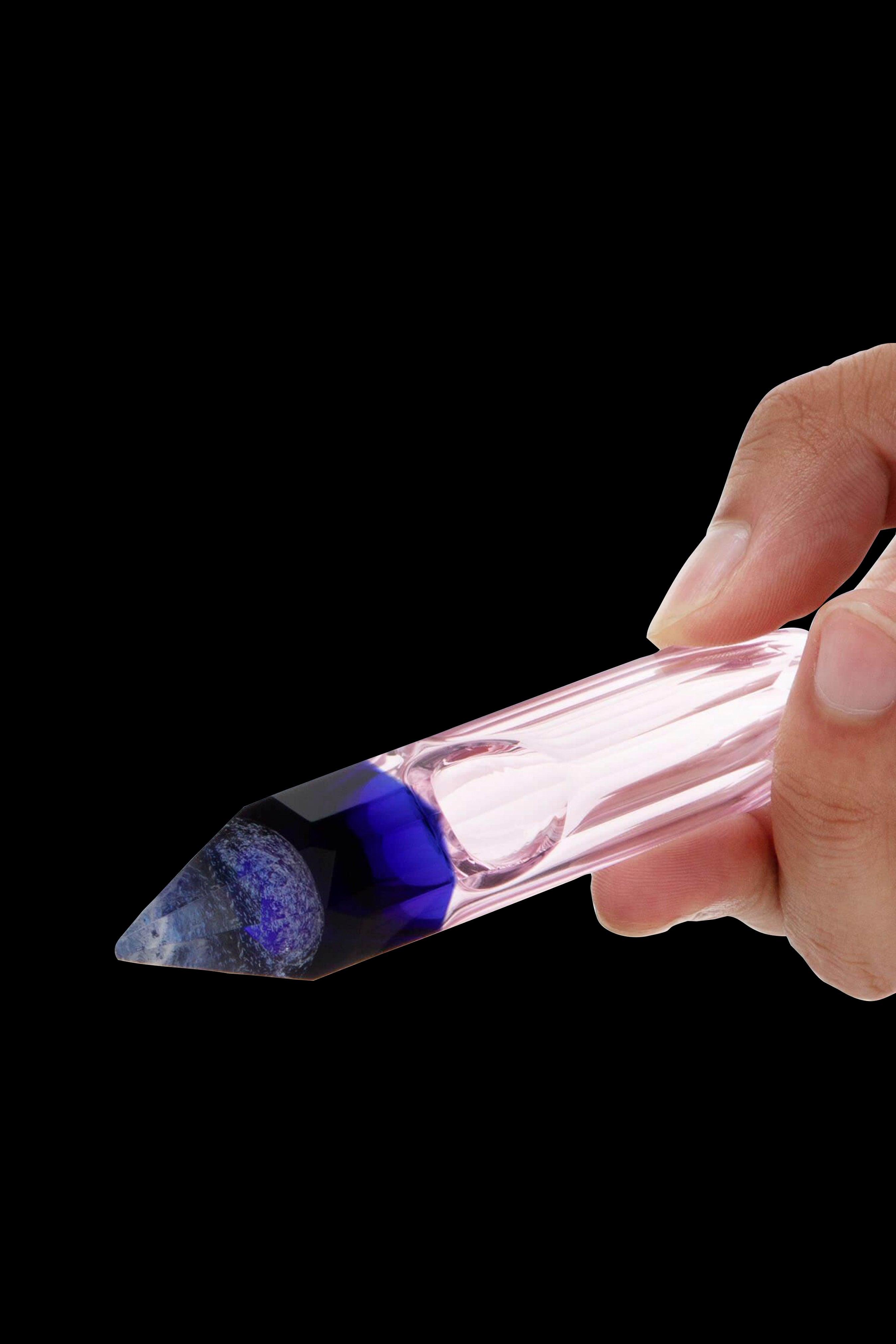 Hand holding a glass cannabis oil burner with a blue-speckled tip.