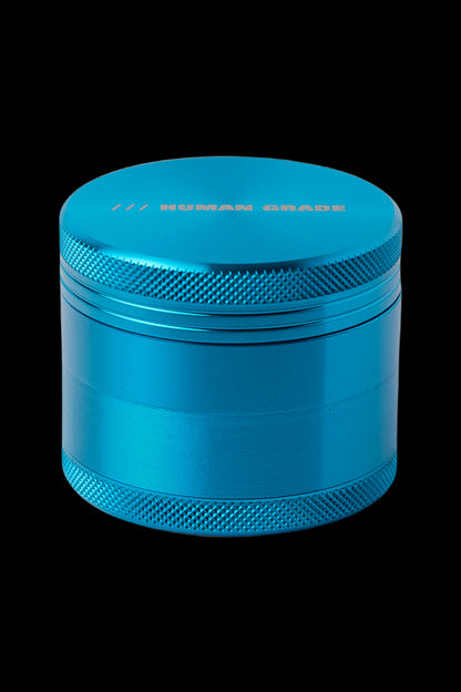 Blue four-piece metal herb grinder with “HUMAN GRADE” text.