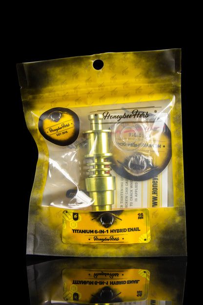 A sealed, silver mylar bag displays a polished, gold-toned titanium 6-in-1 hybrid enail for vaporizing cannabis concentrates, branded with "Honeybee Herb."