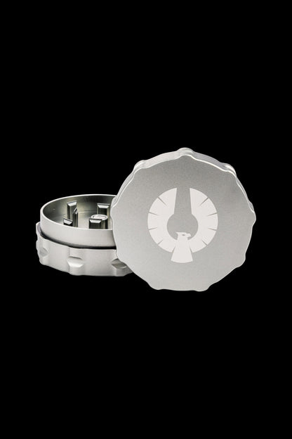 Silver cannabis grinder with a circular design featuring a stylized leaf emblem, open to reveal the internal grinding components.