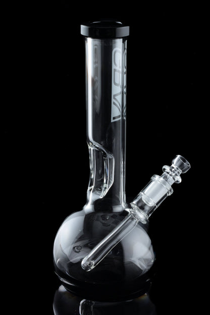 Clear glass water pipe (bong) with a round base and cylindrical neck, reflecting on a dark surface.