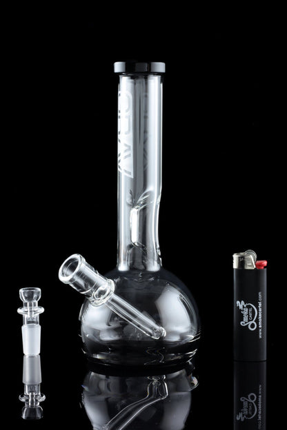 A glass water pipe (bong) with a clear glass bowl and accompanying accessories, reflected on a black surface.