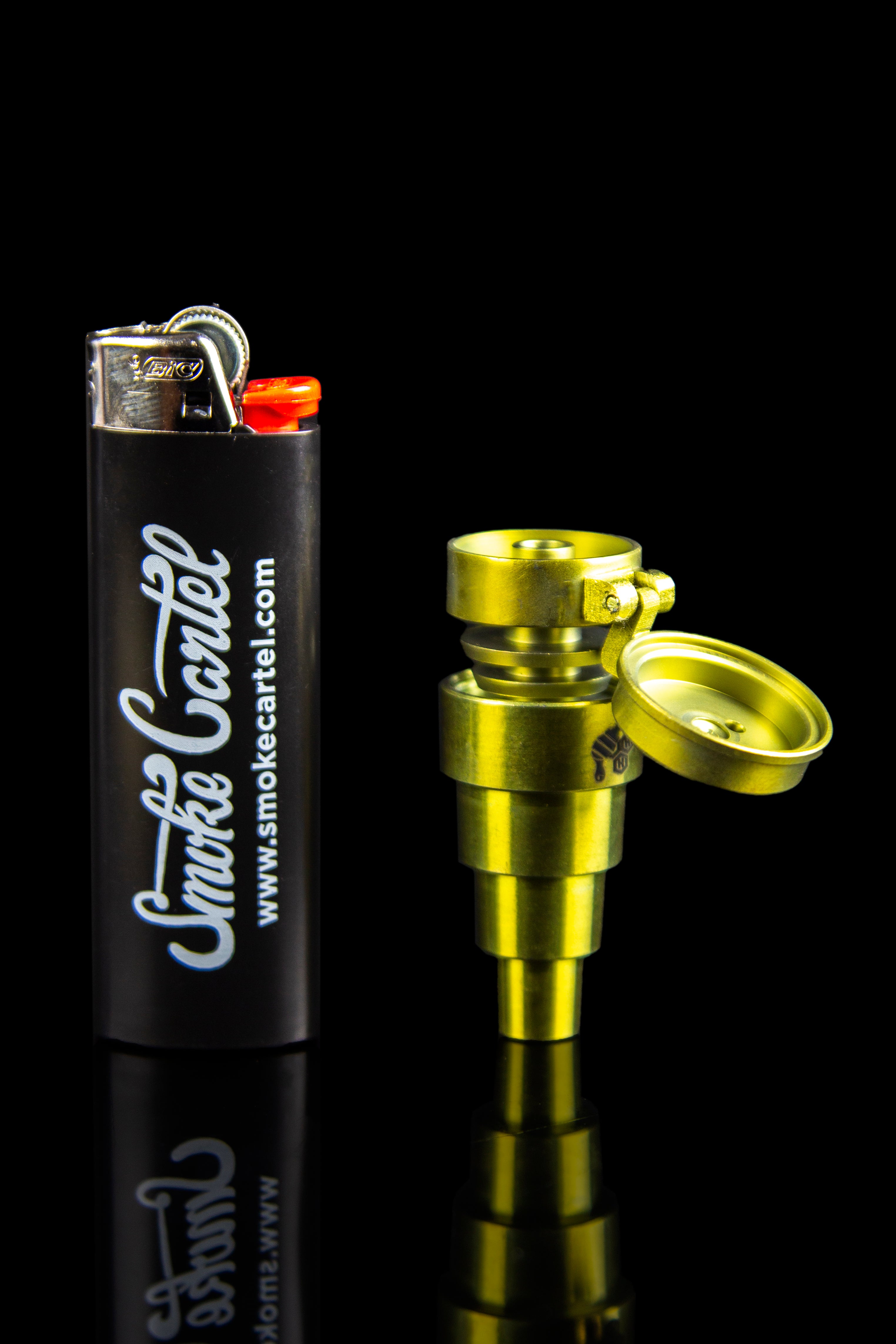 Gold cannabis pipe and lighter with “Smoke Cartel” branding on a black reflective surface.