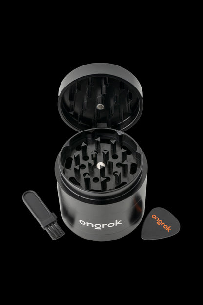 Black metal cannabis grinder with open lid, scraping tool, and small collection dish, branded "onrok."
