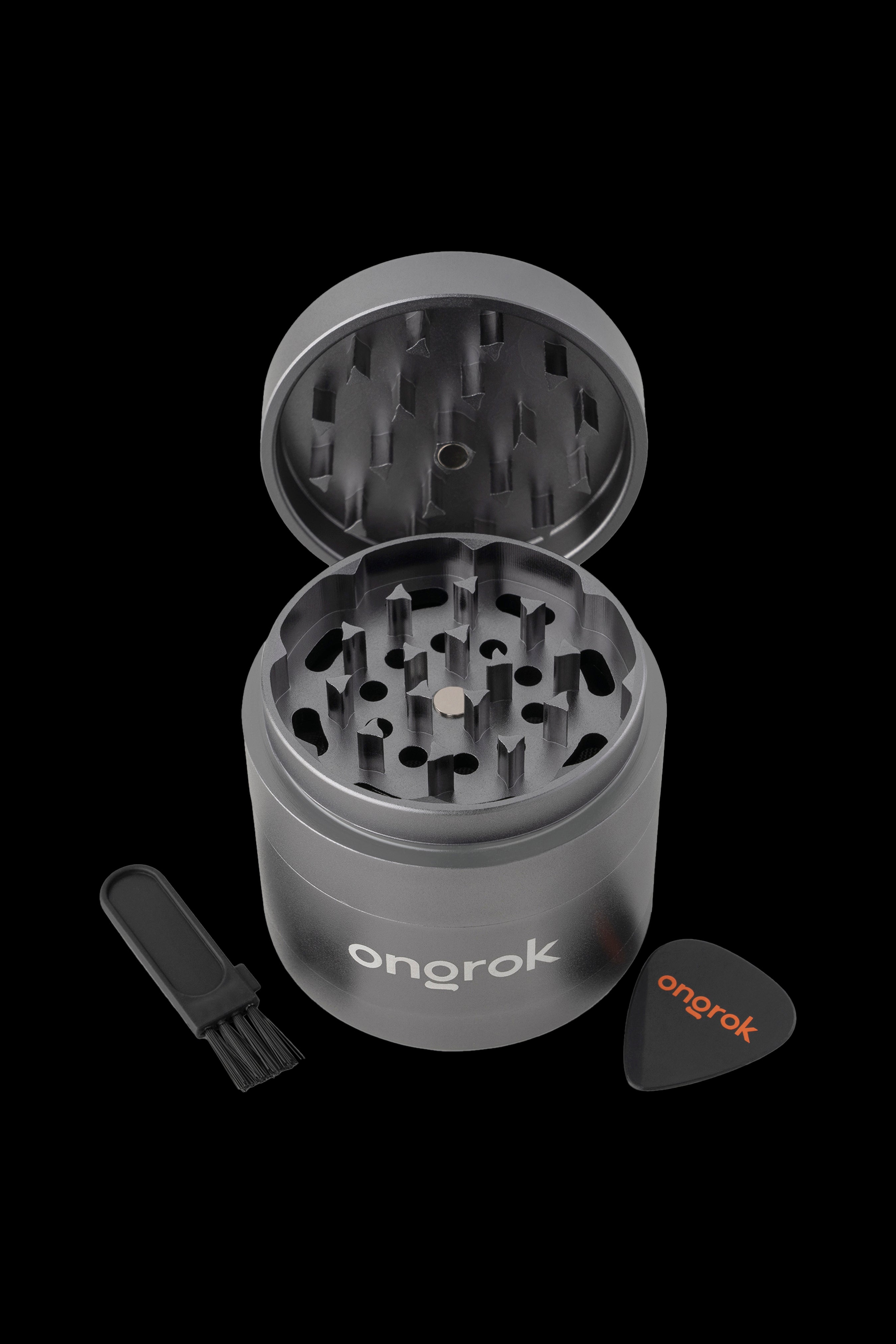 Black metal cannabis grinder with open lid, cleaning brush, and scraper on a dark background.