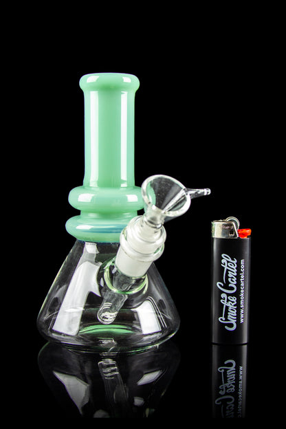 Mint green glass bong with smoke billowing inside, alongside a lighter branded with "Smoke Cartel."