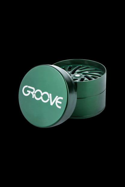 Green metal cannabis grinder with “GROOVE” text on the lid, open to reveal the grinding teeth.