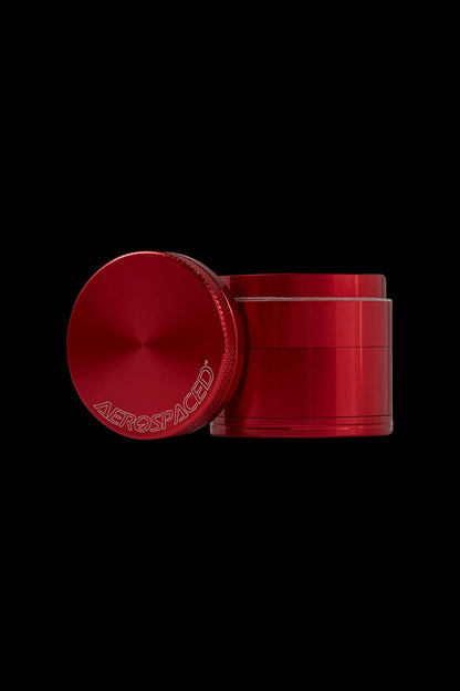 Red four-piece metal grinder with “AEROSPACED” logo, isolated on black.
