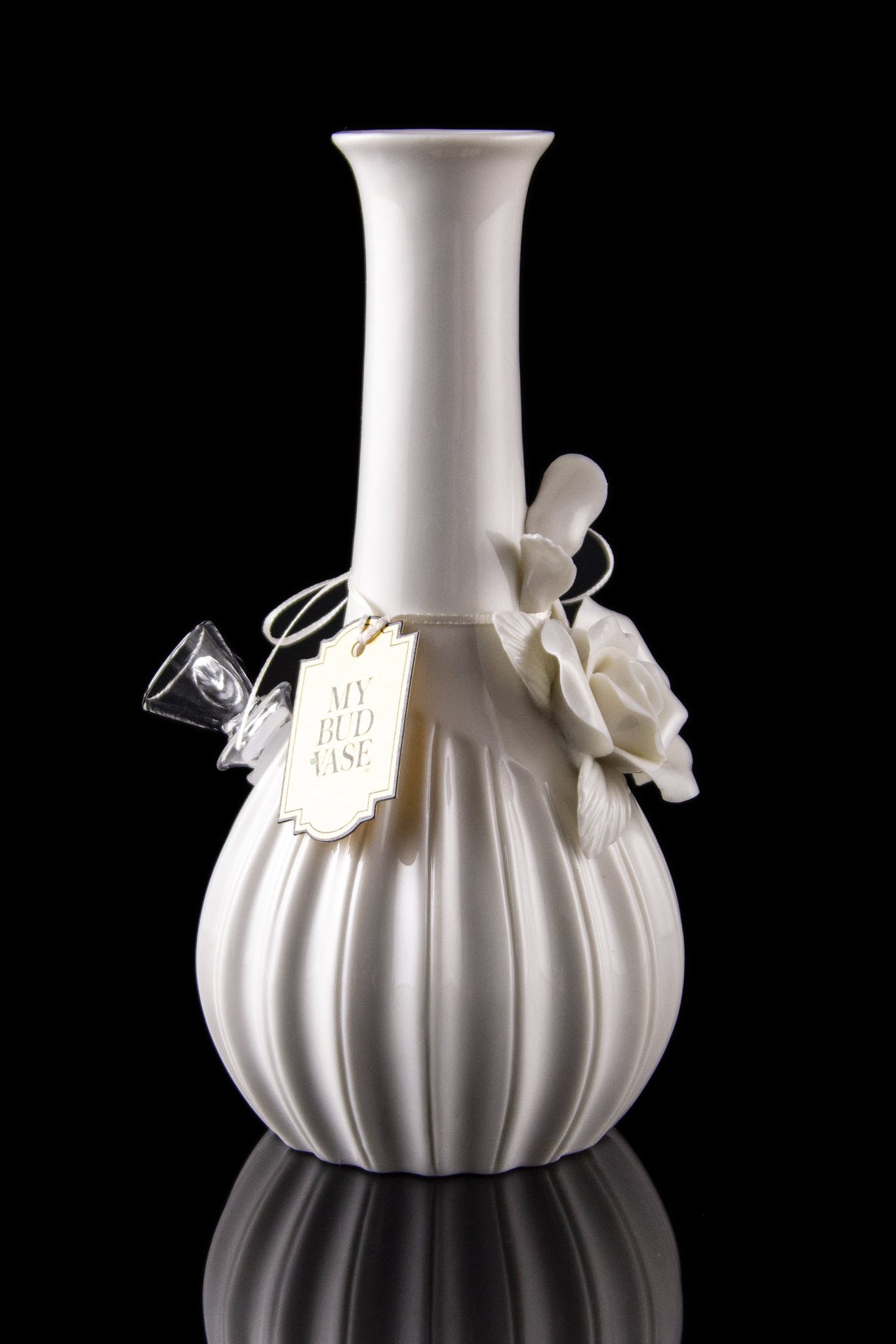 Elegant white glass water pipe with a textured bulbous base and decorative tag, reflected on a dark surface.