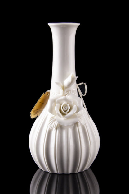 White ceramic bubbler with sculpted roses, reflecting on a black surface.