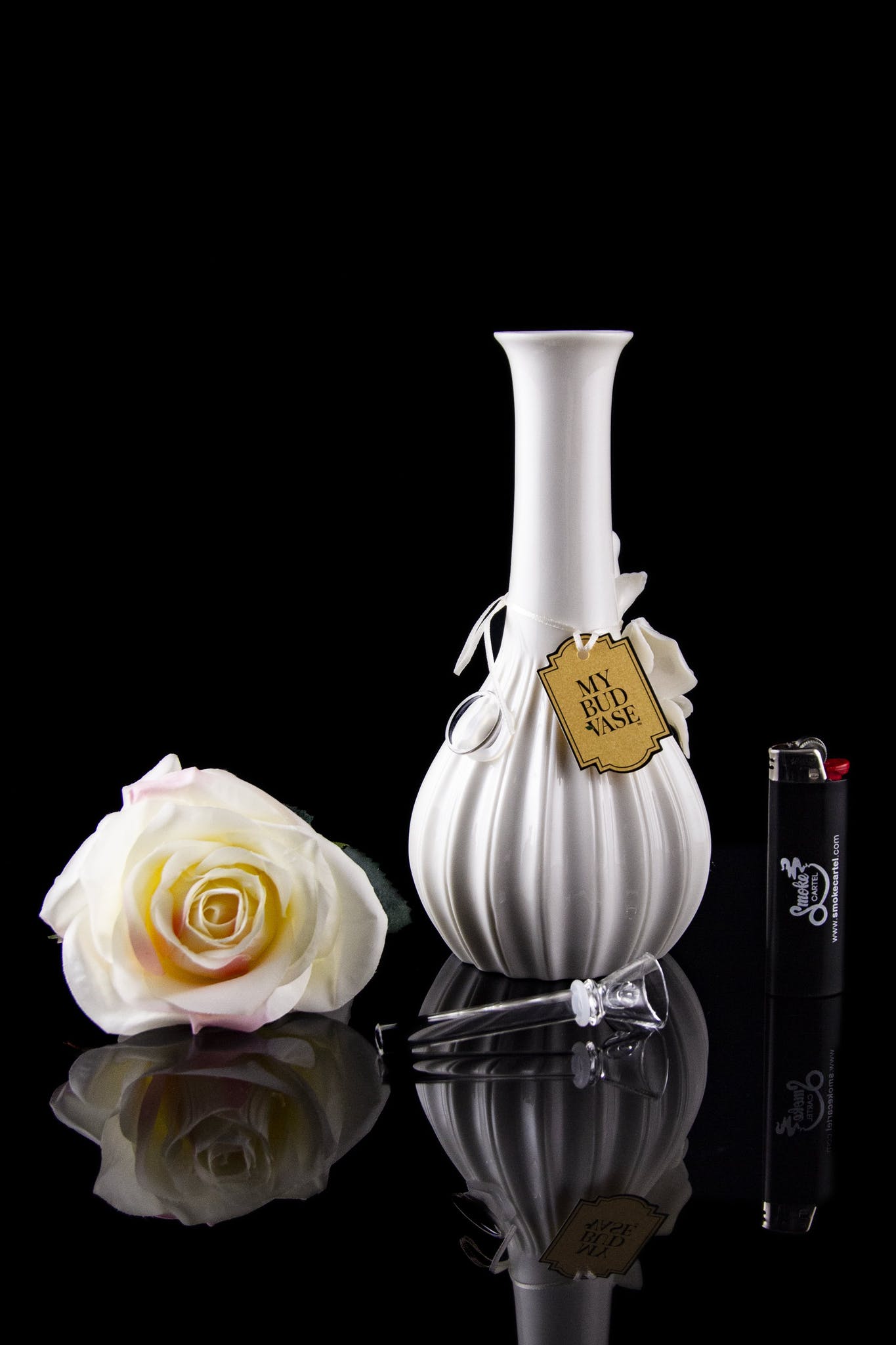 Elegant glass cannabis water pipe with a floral arrangement and lighter, reflected on a glossy black surface.