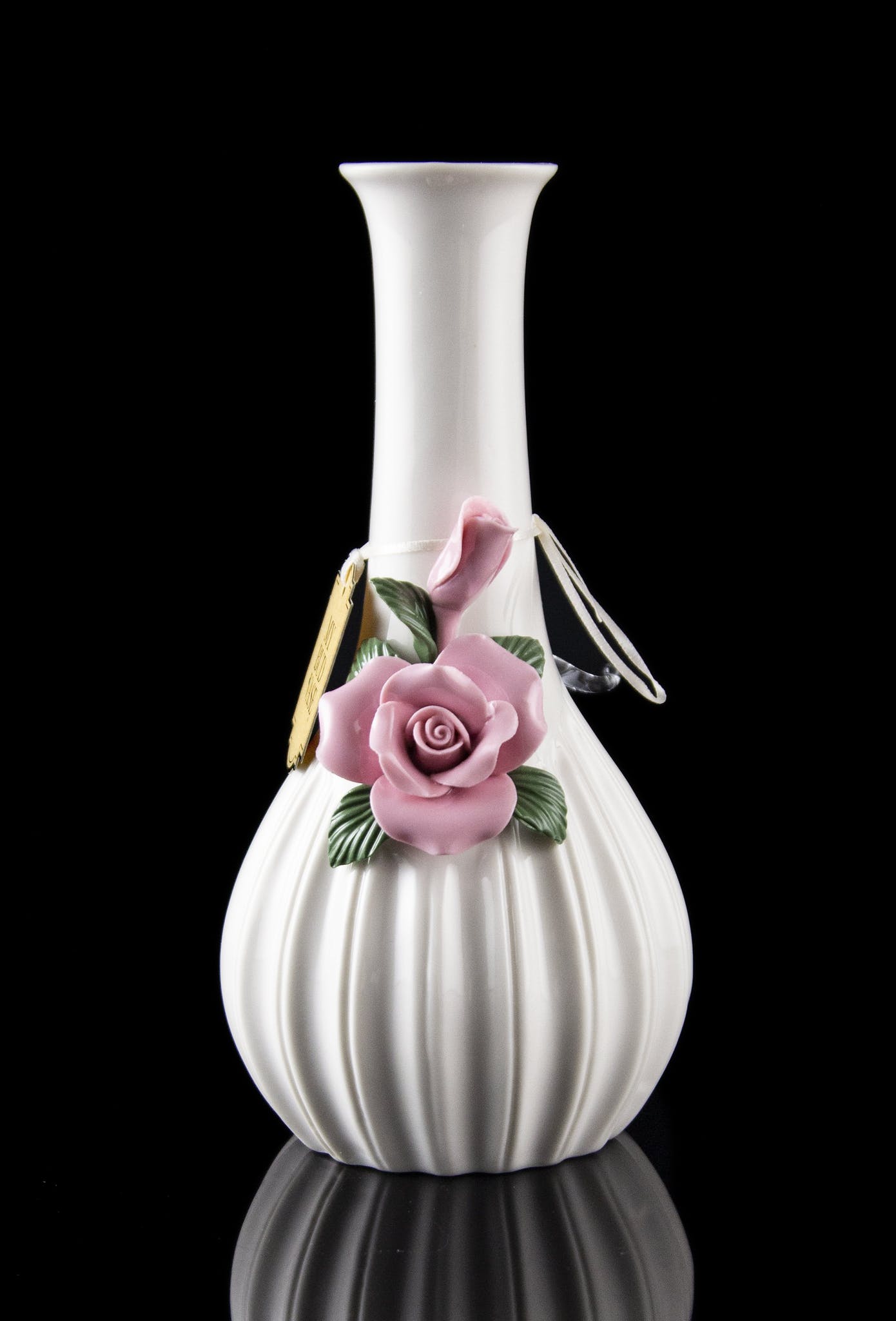 White ceramic bubbler with delicate pink rose embellishment, reflecting on a dark surface.