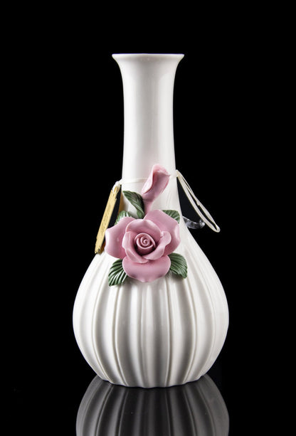 White ceramic bubbler with delicate pink rose embellishment, reflecting on a dark surface.