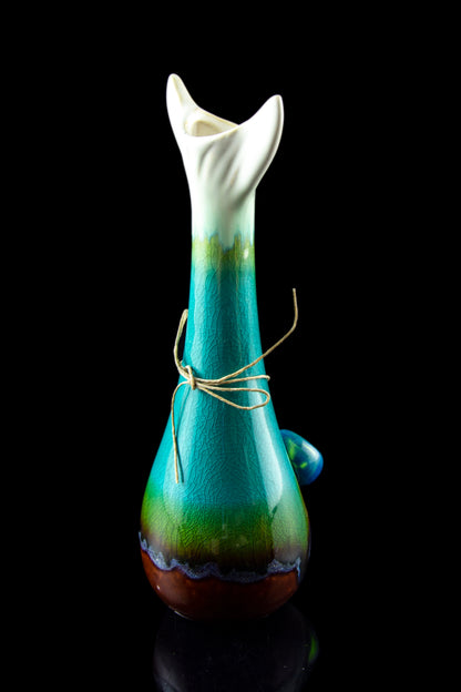 A vibrant green and blue glass water pipe with a rounded base and intricately sculpted neck, tied with natural twine, against a black background.