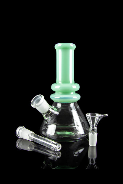 A green glass bong with a conical base and accompanying glass pieces on a reflective surface.