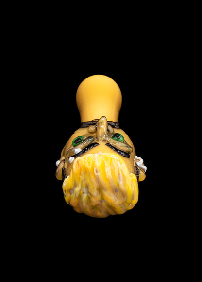 A vibrant, hand-blown glass cannabis water pipe shaped like a stylized monster head with intricate detailing and a yellow, textured body.