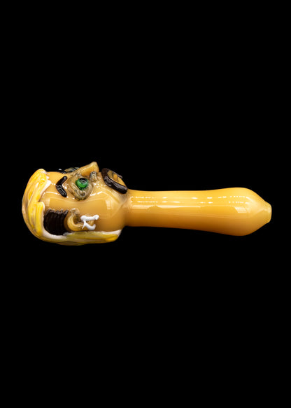 Hand-blown glass pipe shaped like a cartoon monster's head, with green eyes and an open mouth, on a black background.