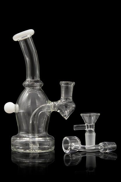 Clear glass bubbler water pipe with accompanying bowl and accessories, reflecting on a dark surface.